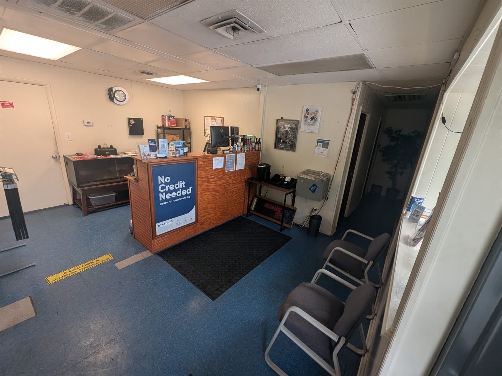 The customer lobby at Zoom Automotive, 2014 12th Street in Lynchburg, Virginia, with the wood reception counter, a Koalafi no credit needed lease-to-own financing sign on the front of it, waiting chairs, and a water cooler